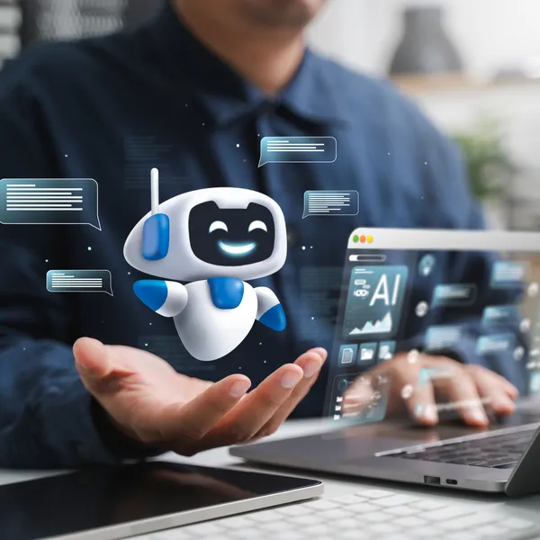 Person arbeitet an einem Laptop mit schwebender, lächelnder Roboterfigur und Chatfenstern in der Hand; AI-bezogenes Interface auf dem Bildschirm.
