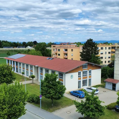 Luftaufnahme der Kanzleigebäude in Straubing, mit rotem Dach, umgeben von Bäumen, Straßen und geparkten Autos an einem bewölkten Tag.