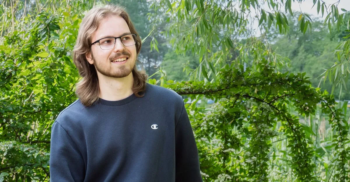 Sampo standing outdoors among green willow branches, smiling and looking off to the side