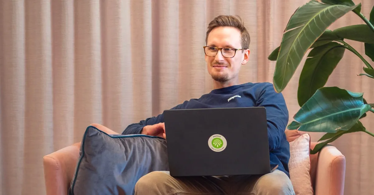 Aleksi sitting in an armchair with a laptop bearing a Digisalix sticker on his lap, a plant in the background