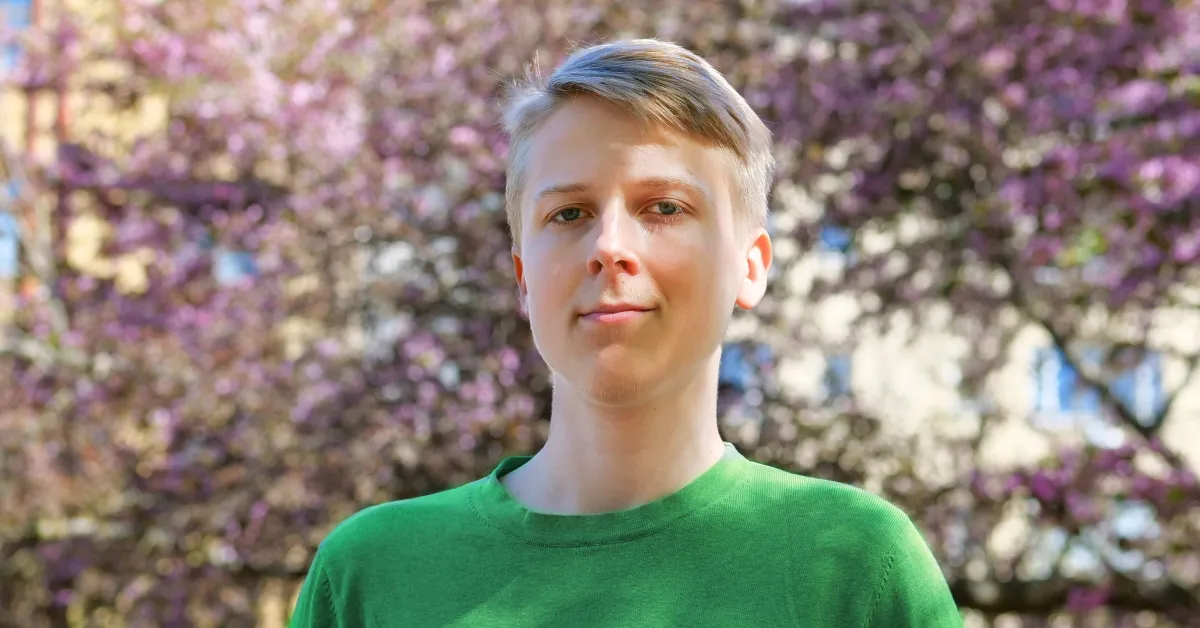 Portrait of Väinö, Digisalix's summer trainee, standing outdoors in a green t-shirt in front of blossoming pink cherry trees