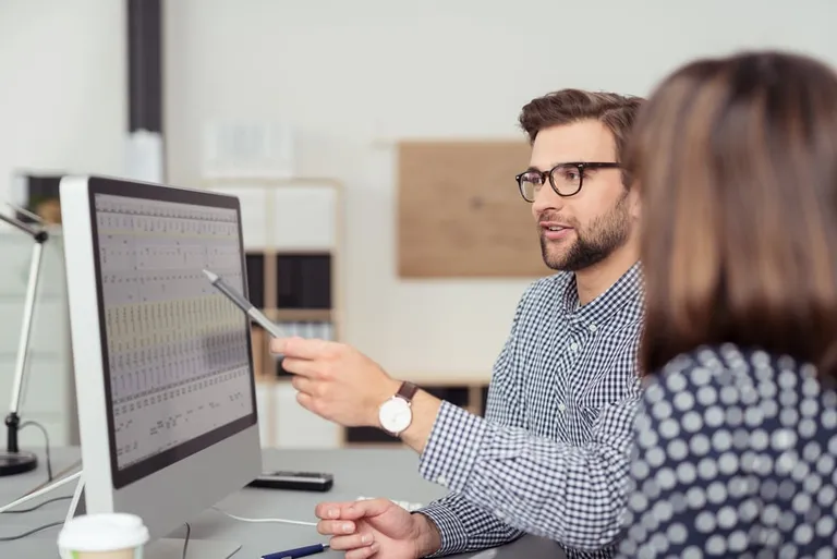 Employee discussing a business analysis with a colleague at a computer in an office