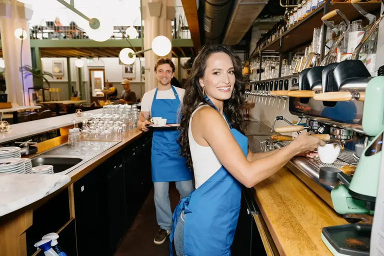 Two staff members behind a café bar, one of them pulling a coffee