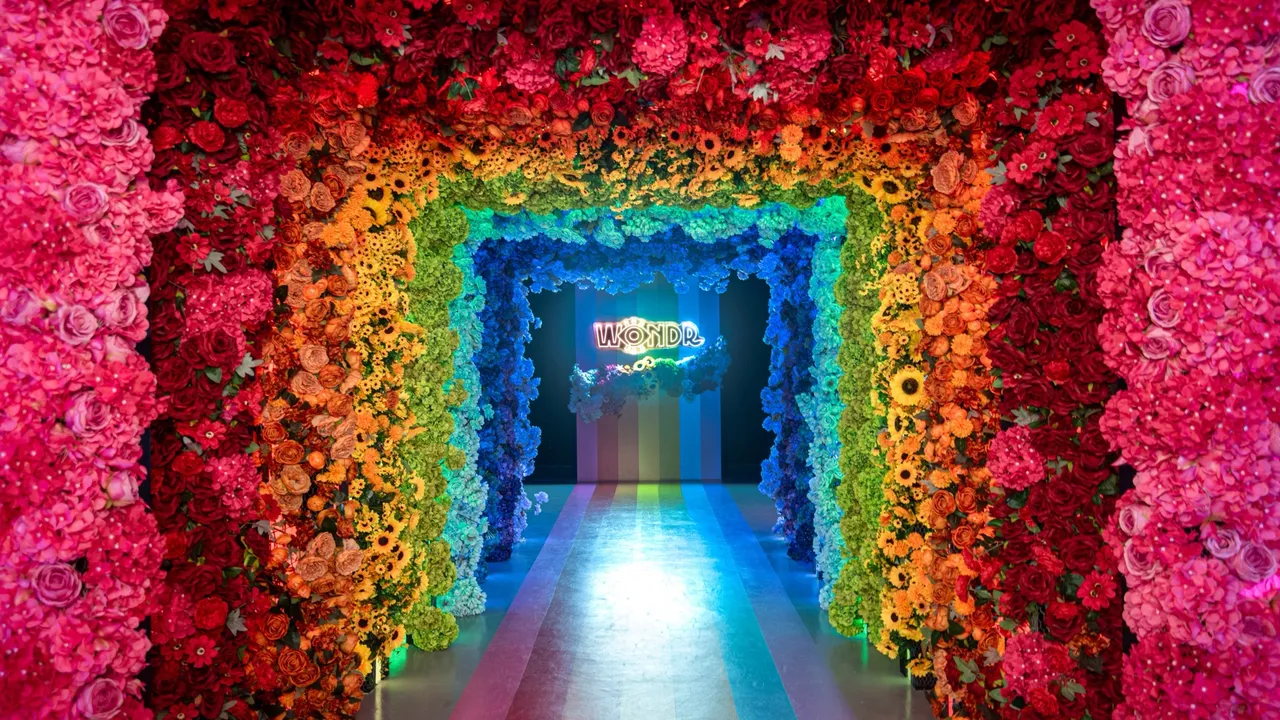 Bloemenboog in regenboogkleuren met het WONDR-neonbord bij WONDR Experience in Amsterdam