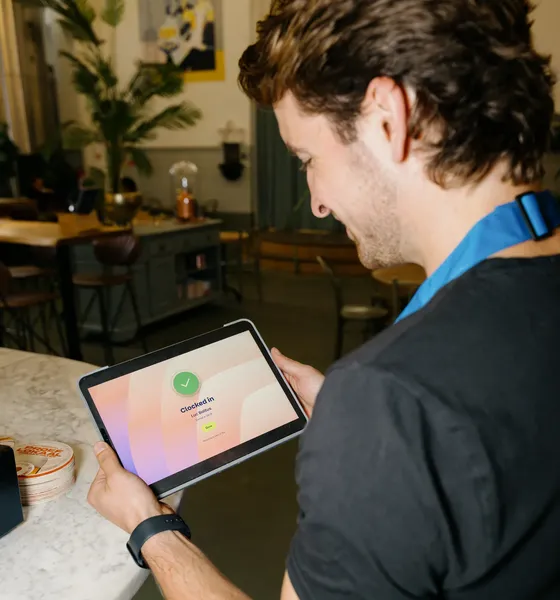 Waiter in a blue apron clocking in on a tablet in a café