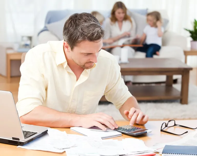 Homme calculant ses factures pendant que sa famille est assise sur le canapé