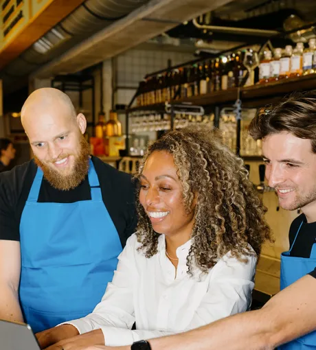 Twee medewerkers kijken mee terwijl een manager op de laptop werkt aan de bar