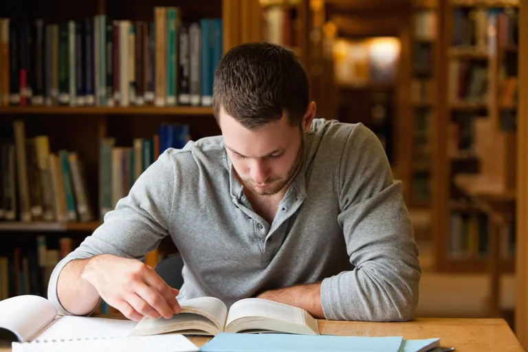 Un étudiant fait des recherches avec un livre dans une bibliothèque