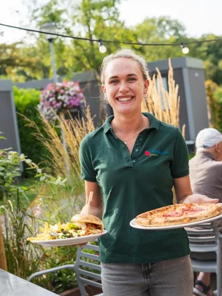 Server with pizzas on the terrace at Vakantiepark Delftse Hout