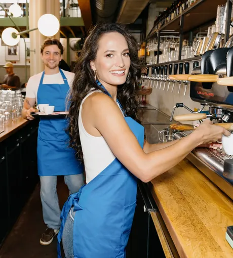 Barista making a coffee at the bar while a colleague serves