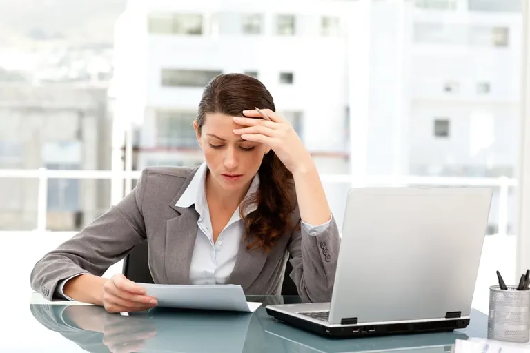 Pensive businesswoman looking at a paper while working on her laptop à son bureau