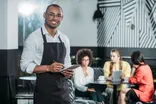 Ein Kellner mit Tablet in einem Café, im Hintergrund sitzen Gäste an Tischen