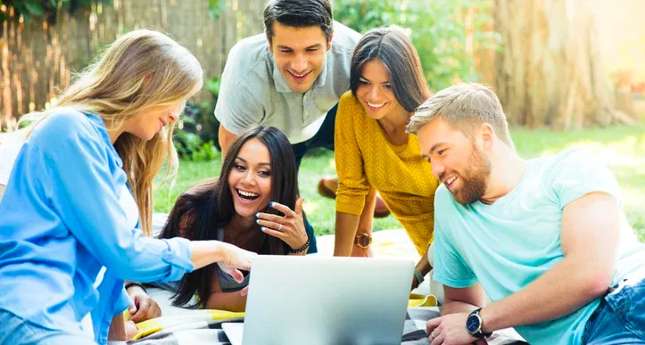 Groep jonge collega’s die buiten samen naar een laptop kijken.