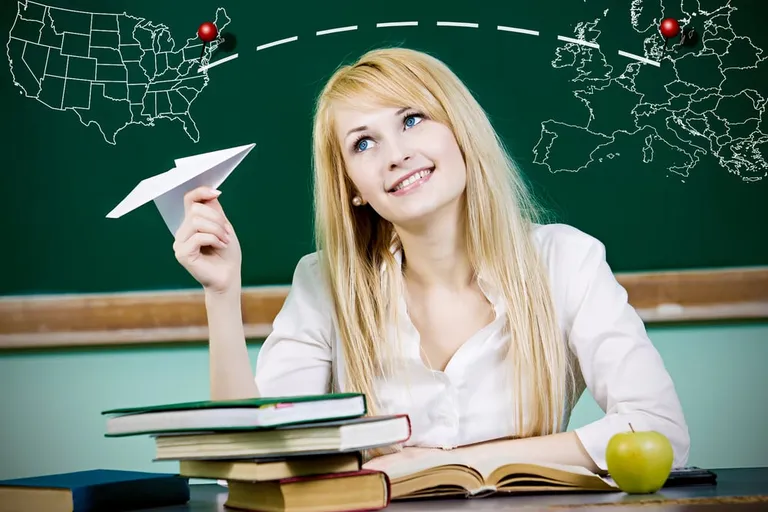 Femme souriante tenant un avion en papier devant un tableau vert avec une carte du monde