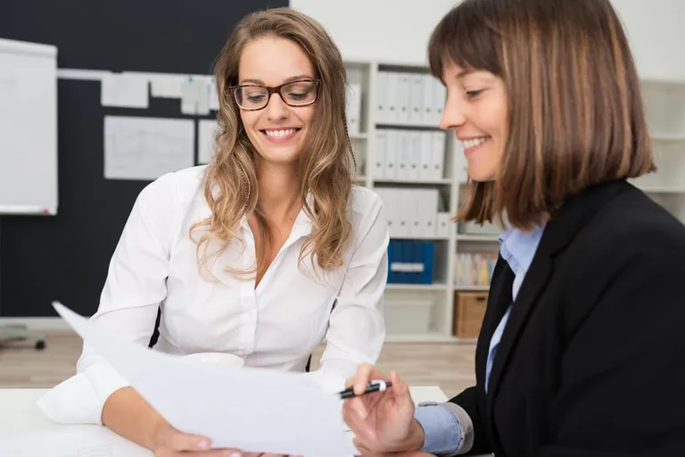 Deux jeunes femmes souriantes au bureau discutent d’un rapport papier