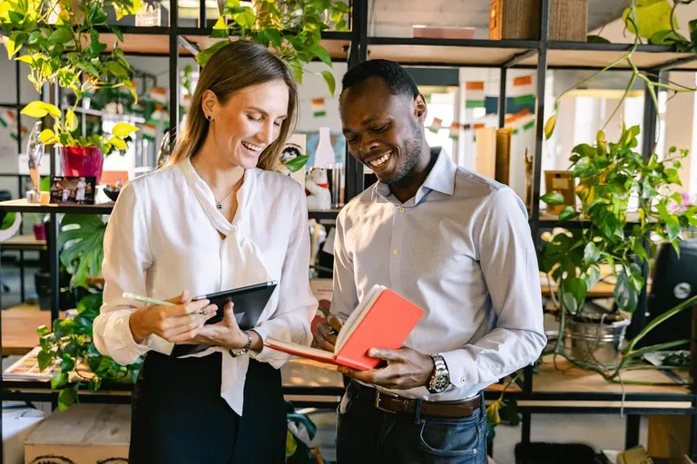 Two employees looking at project notes in a red notebook