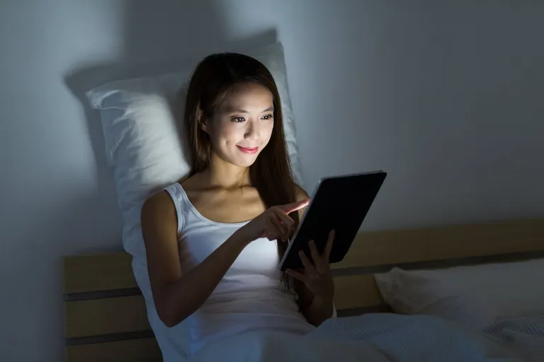 Femme travaillant de nuit avec une tablette assise sur un lit
