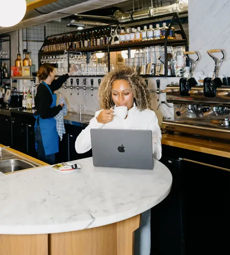An owner with a coffee and her laptop at the end of the bar, a colleague working behind her