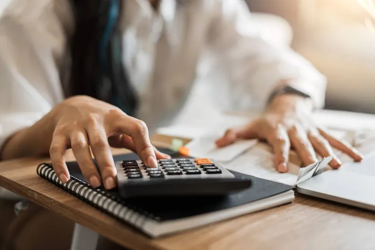 Woman using calculator and note to calculate income or expenses