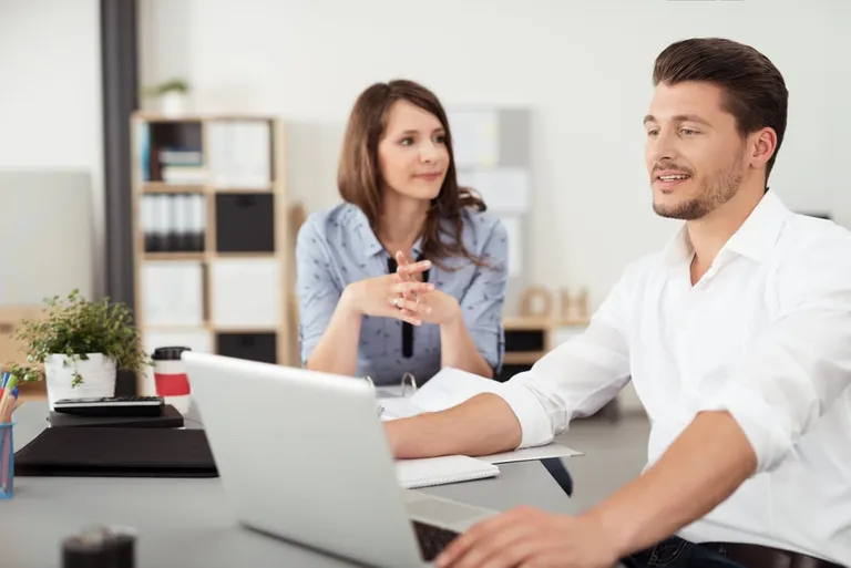 Deux jeunes collègues discutent travail, assis à une table du bureau