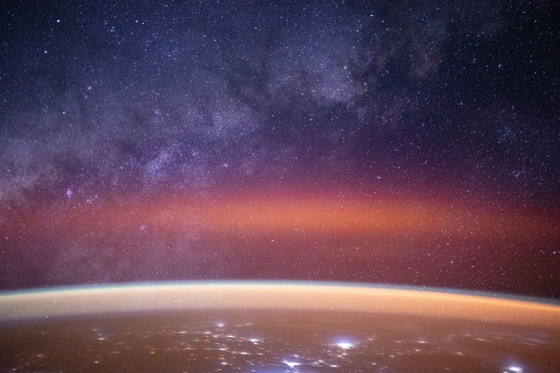 De Melkweg en een rode gloed boven de nachtelijke aarde, gezien vanuit het ruimtestation ISS