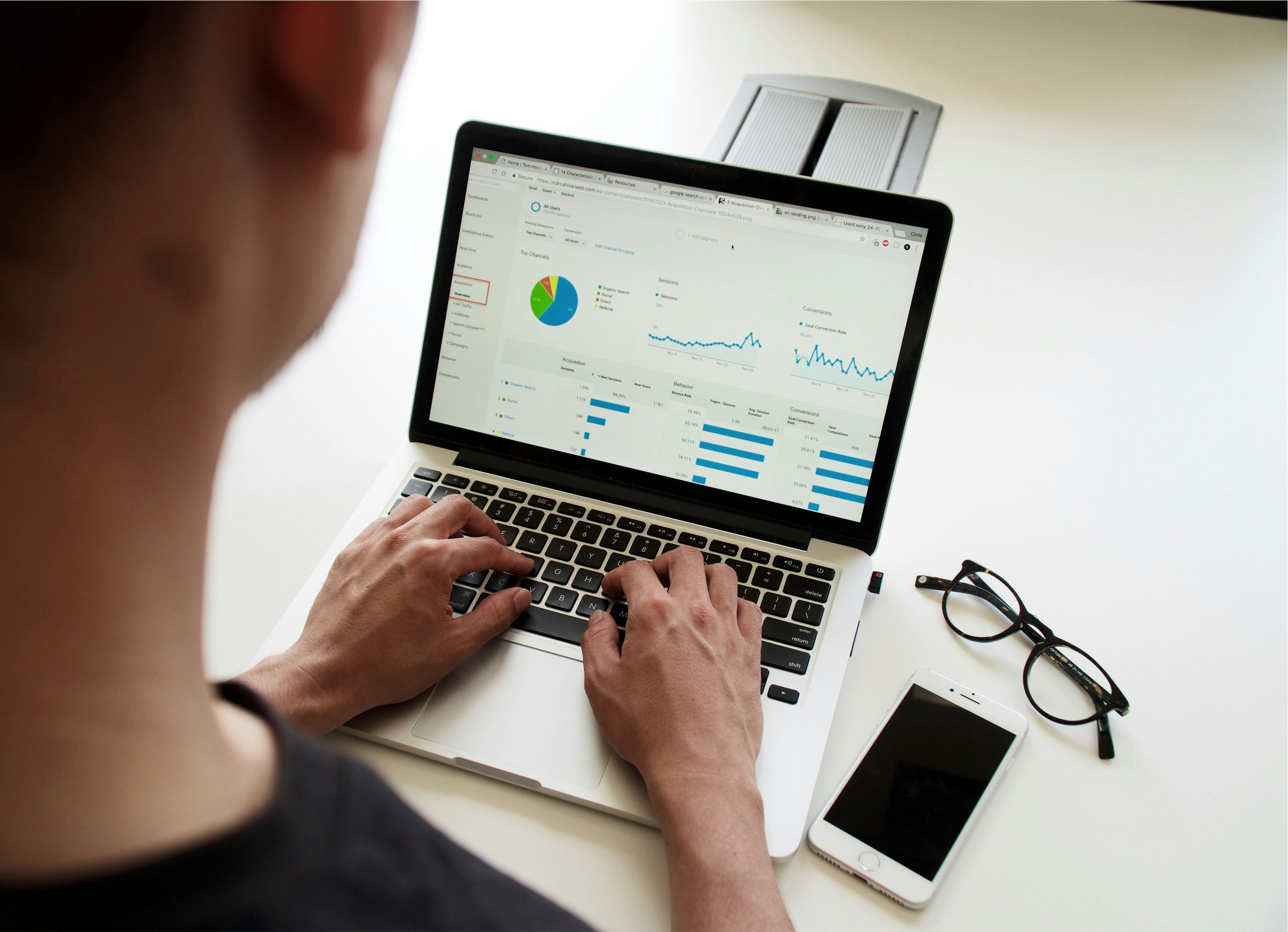 Person typing on a laptop displaying a website analytics dashboard with traffic sources, session trends, and conversion rate charts