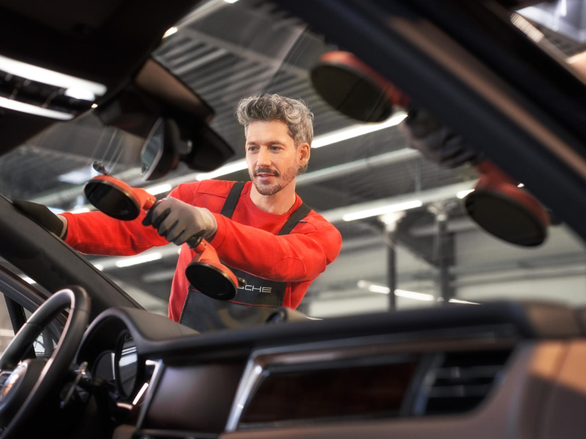 Ein Porsche Mitarbeiter setzt eine neue Frontscheibe ein.