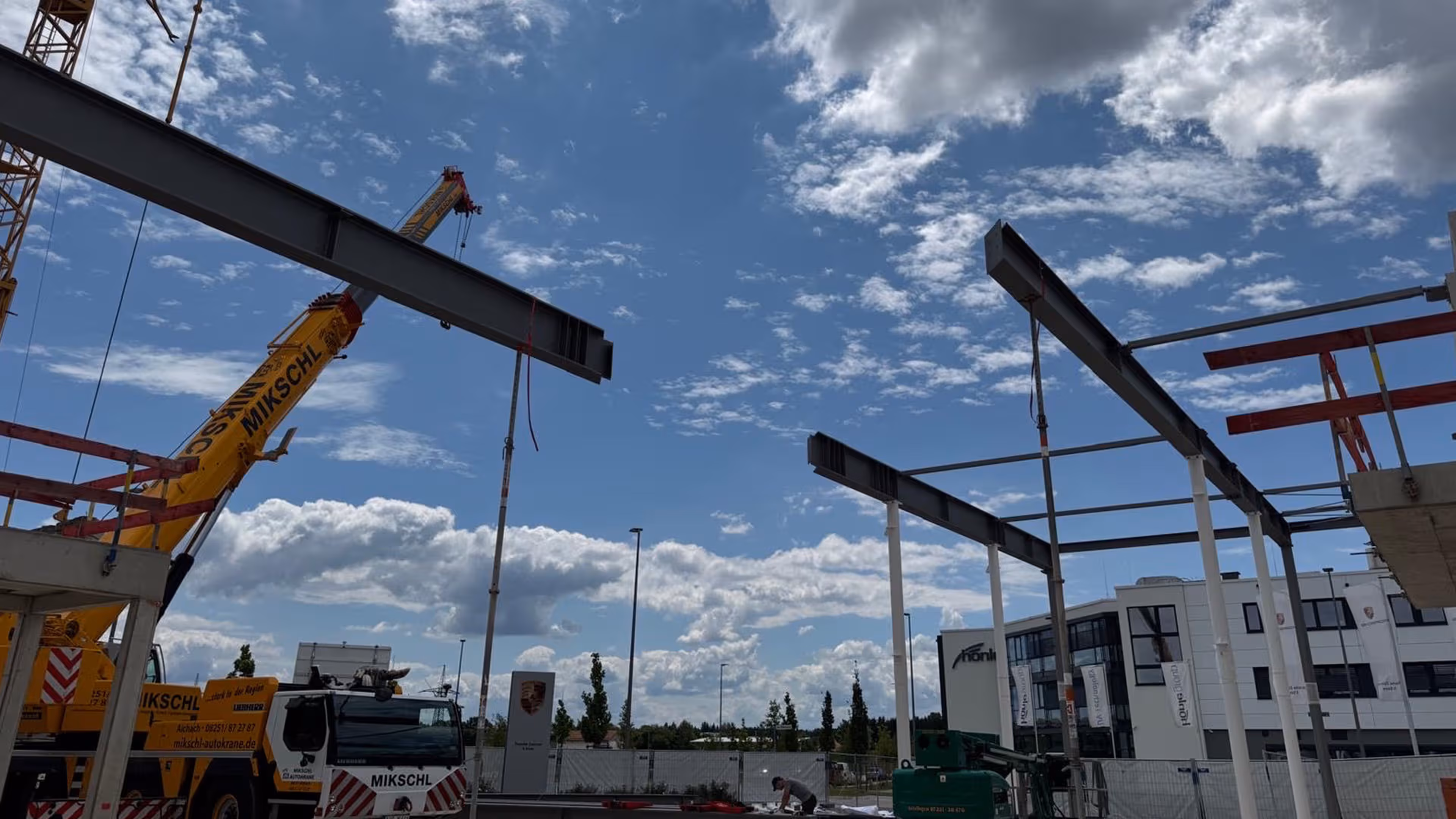 Baustelle mit gelbem Kran, Stahlträgern und Gebäuden unter bewölktem Himmel.