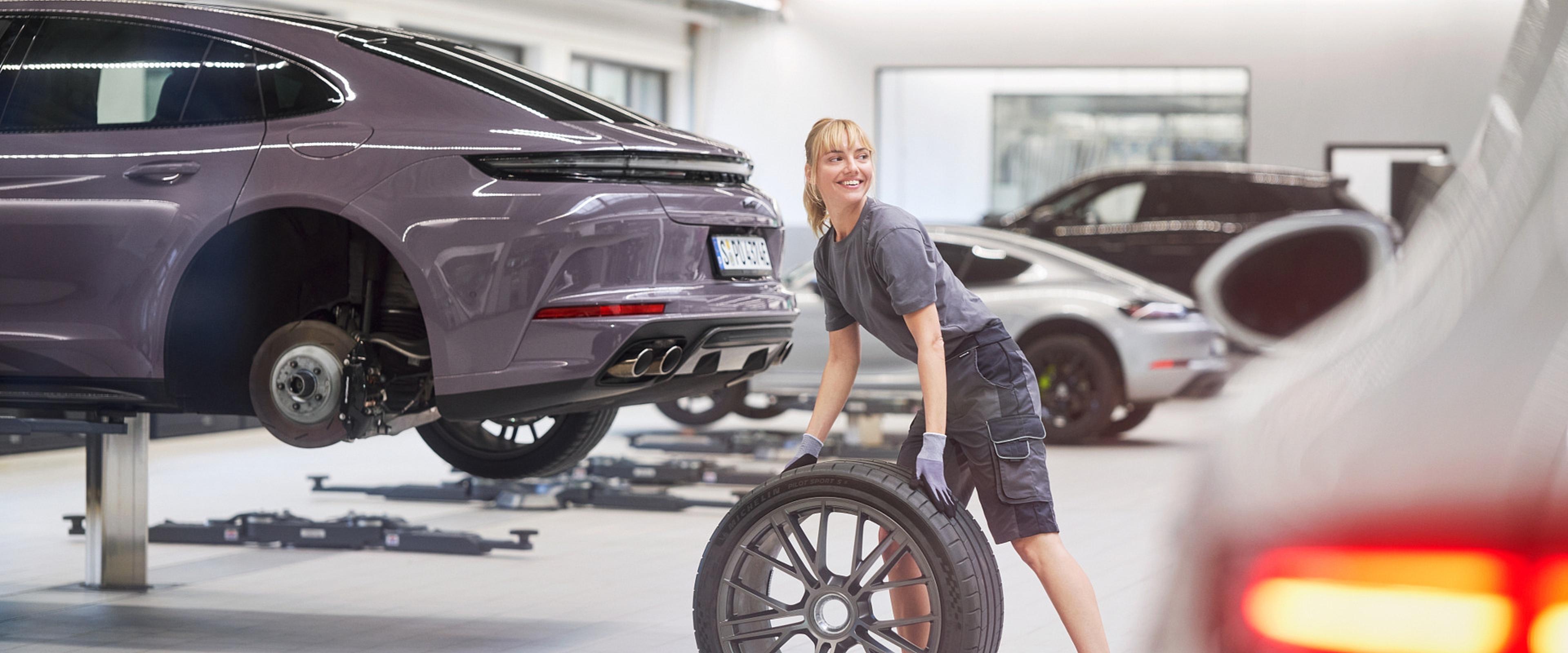 Eine Porsche Werkstattmitarbeiterin wechselt die Reifen eines Porsche Sportwagens.