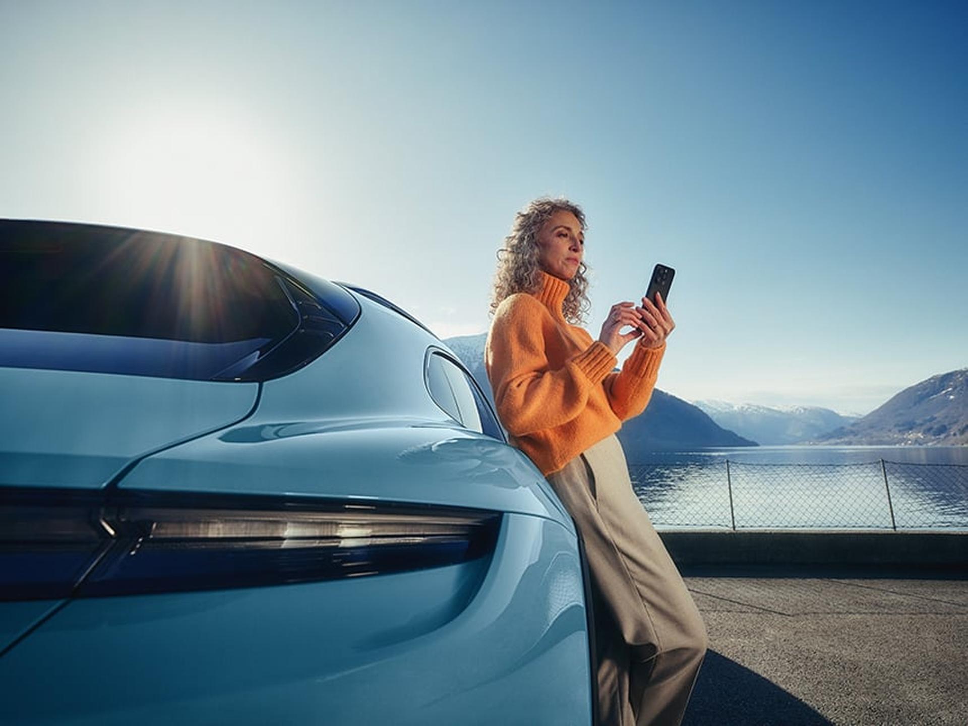Ein Porsche Fahrerin lehnt mit ihrem Handy an ihrem Porsche Sportwagen.