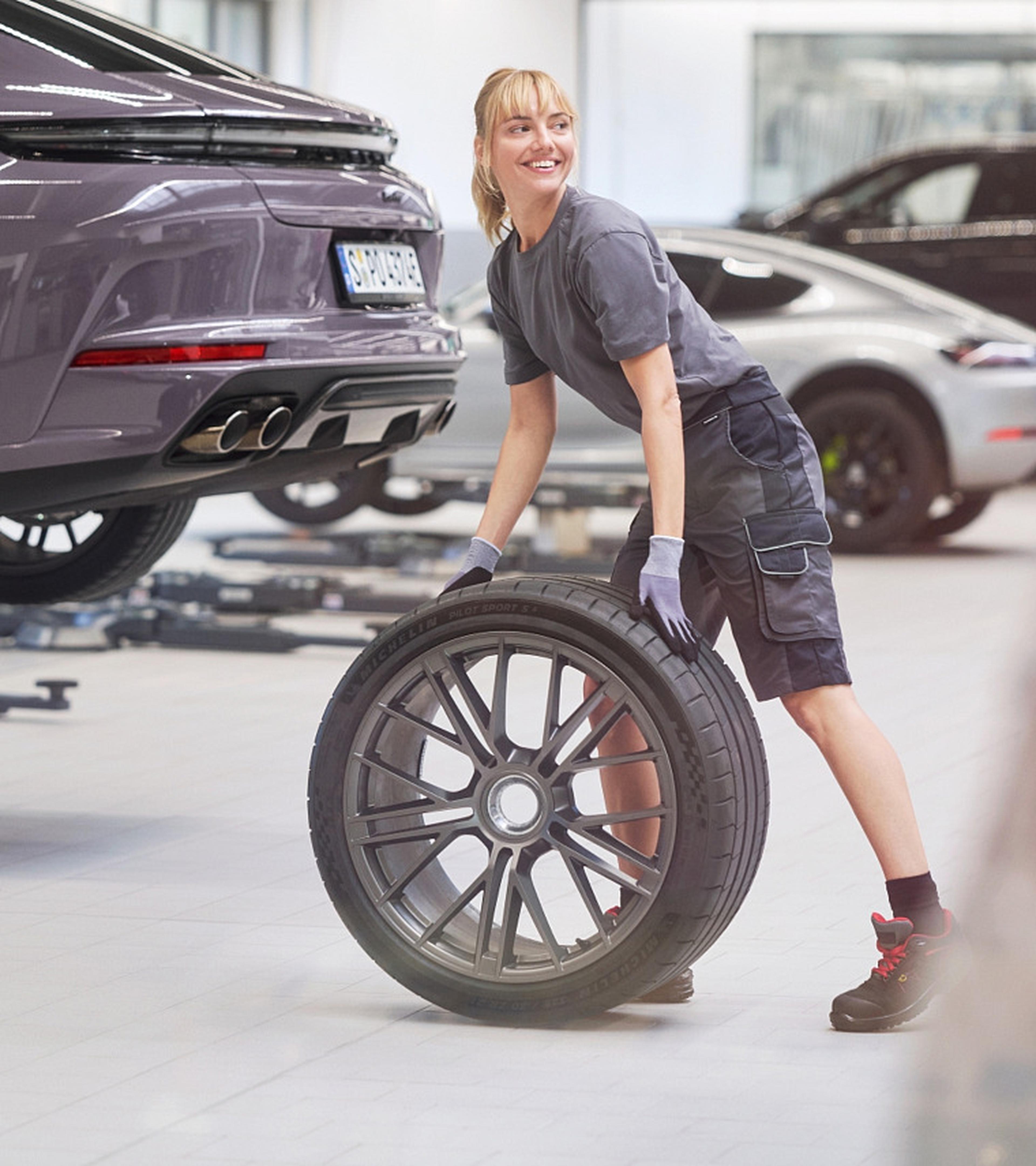 Eine Porsche Werkstattmitarbeiterin wechselt die Reifen eines Porsche Sportwagens.