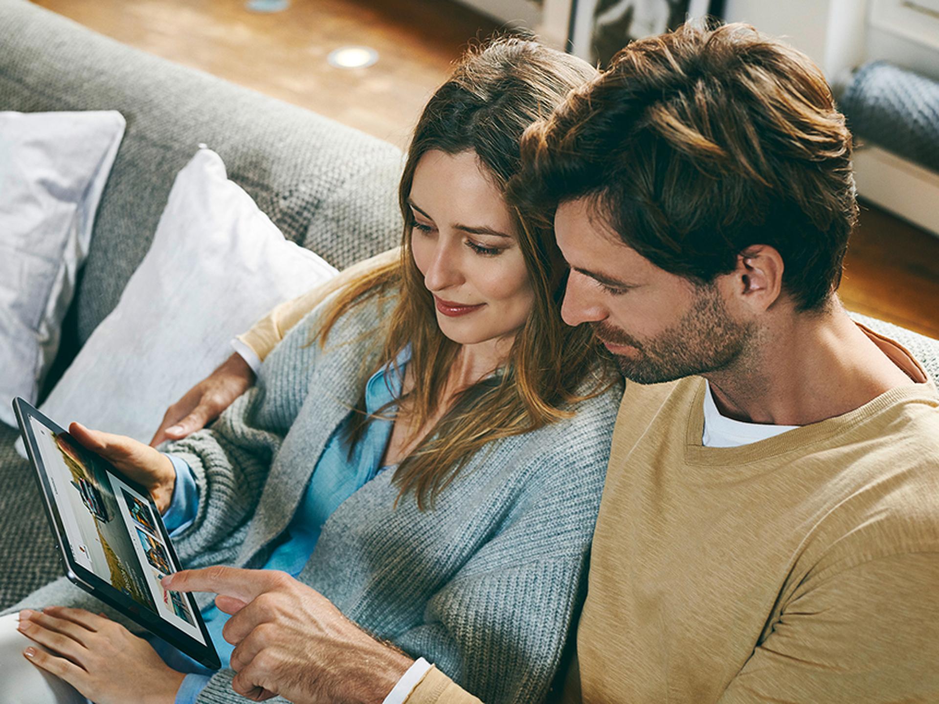 Frau und Mann sitzen auf dem Sofa und schauen gemeinsam in ein Tablet.