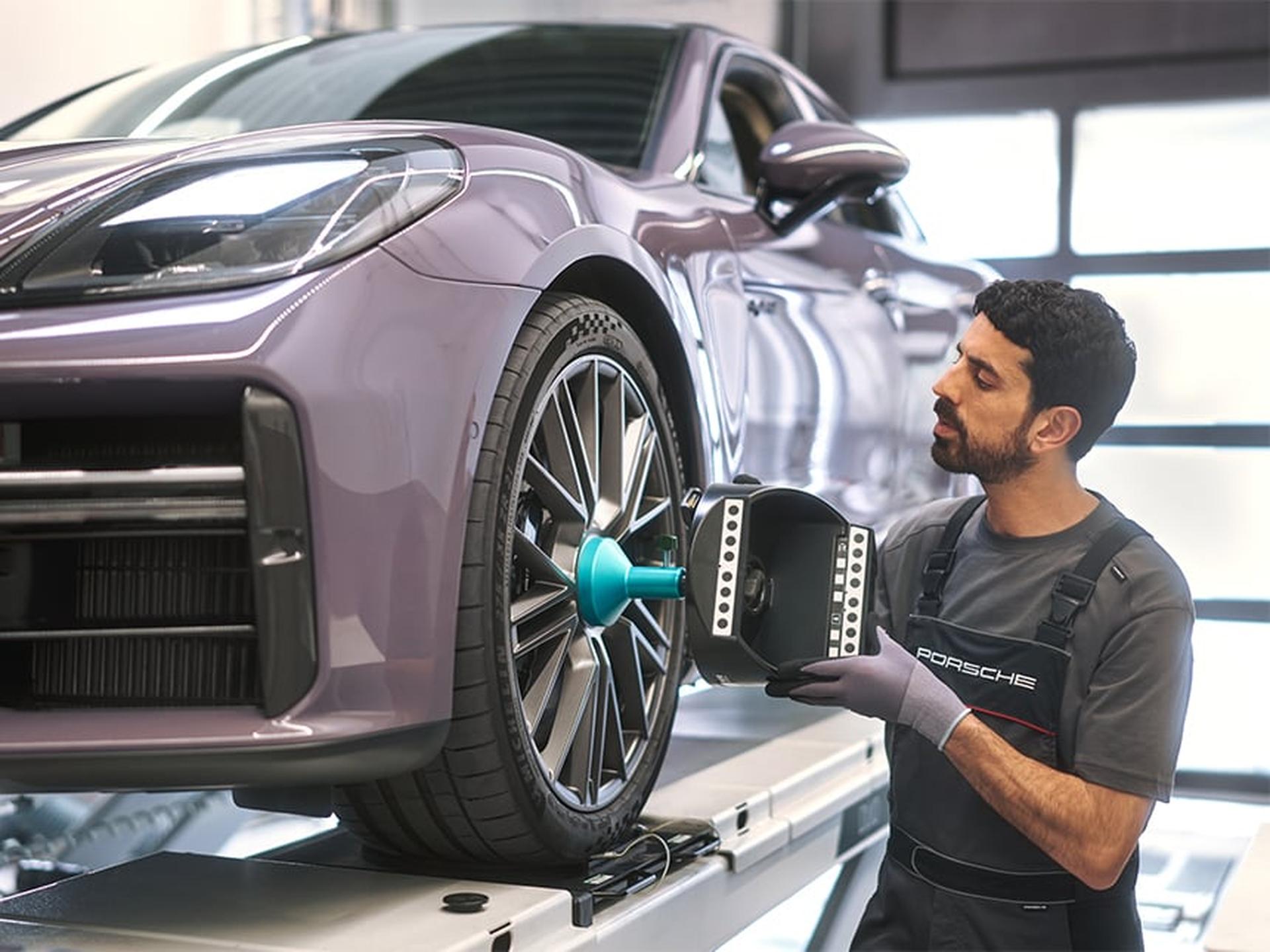 Ein Porsche Servicemitarbeiter führt in der Werkstatt eine Achsvermessung an einem Porsche Sportwagen durch.