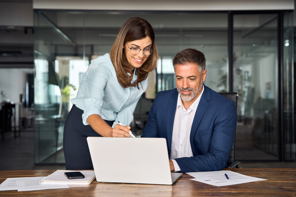 Eine Businessfrau zeigt einem Businessmann etwas auf einem aufgeklapptem Laptop-Bildschirm.