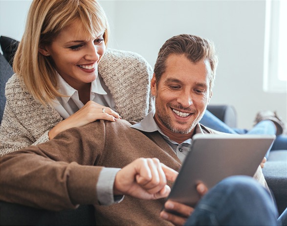 Ein junges Paar im Wohnzimmeratmosphäre nutzt gemeinsam ein Tablet für digitale Medien und Nachrichten.