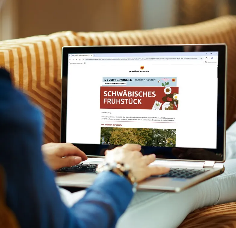 Eine Frau sitzt mit ihrem Laptop auf dem Sofa und sieht auf ihrem Bildschirm den Newsletter von schwaebische.de "Schwäbisches Frühstück"