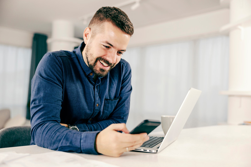 Ein Mann nutzt mehrere Medienkanäle und digitale Geräte wie beispielsweise Smartphone und Laptop häufig gleichzeitig, wie hier auch ein Mann bei der Nutzung seines Handys und Laptops zu sehen ist.