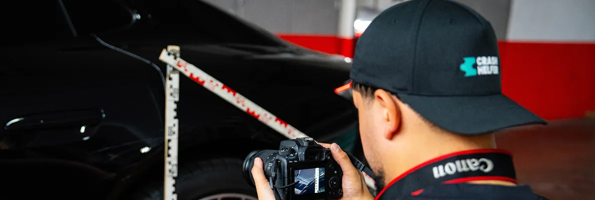 Gutachter fotografiert die Seite eines schwarzen Autos mit angelegtem Zollstock