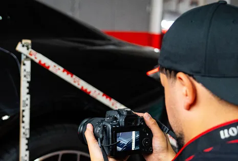 Gutachter fotografiert die Seite eines schwarzen Autos mit angelegtem Zollstock