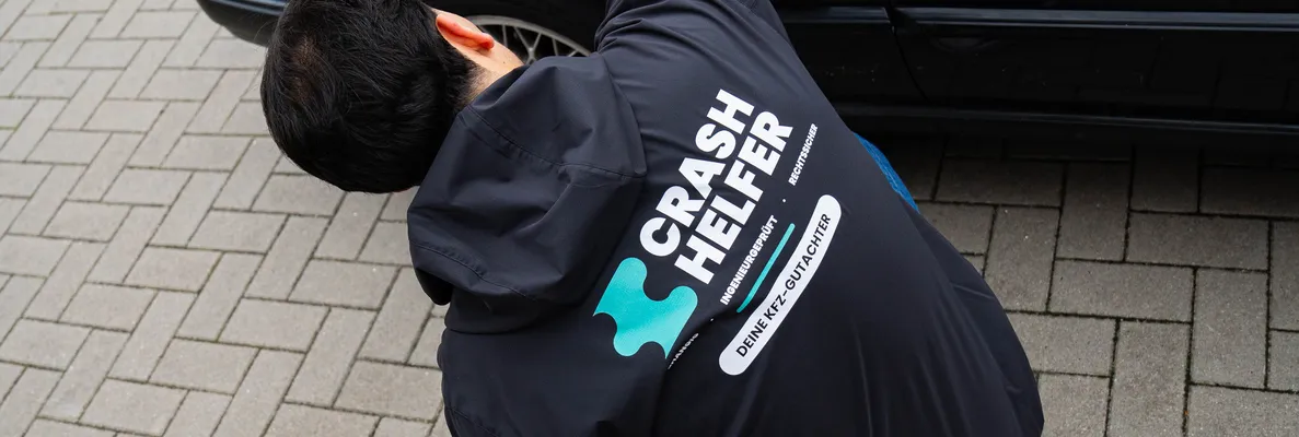 Gutachter prüft den Kotflügel eines schwarzen BMW, daneben Koffer und Gutachtenmappe