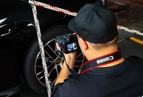 Gutachter fotografiert den Radkasten eines schwarzen Autos mit angelegtem Zollstock