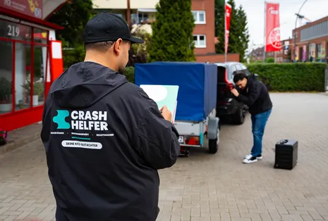Zwei Crash Helfer Gutachter besichtigen ein Auto mit Anhänger auf einem Hof