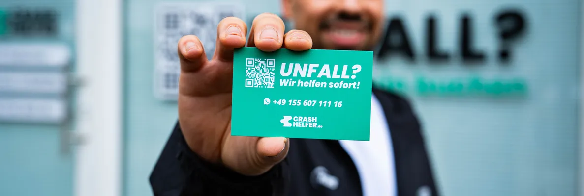 Crash Helfer Mitarbeiter hält eine Karte mit der Notfallnummer +49 155 60711116 in die Kamera