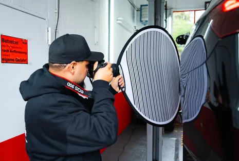 Gutachter prüft den Lack eines Autos mit einer Streifentafel, die kleine Dellen sichtbar macht