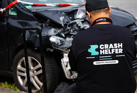 Crash Helfer Gutachter vor einem Unfallwagen mit stark zerstörter Front