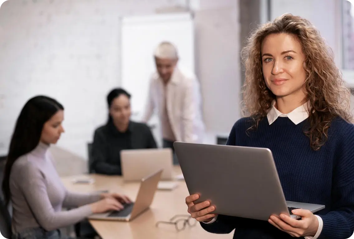 Team working in a meeting room, with a colleague holding a laptop in the foreground.