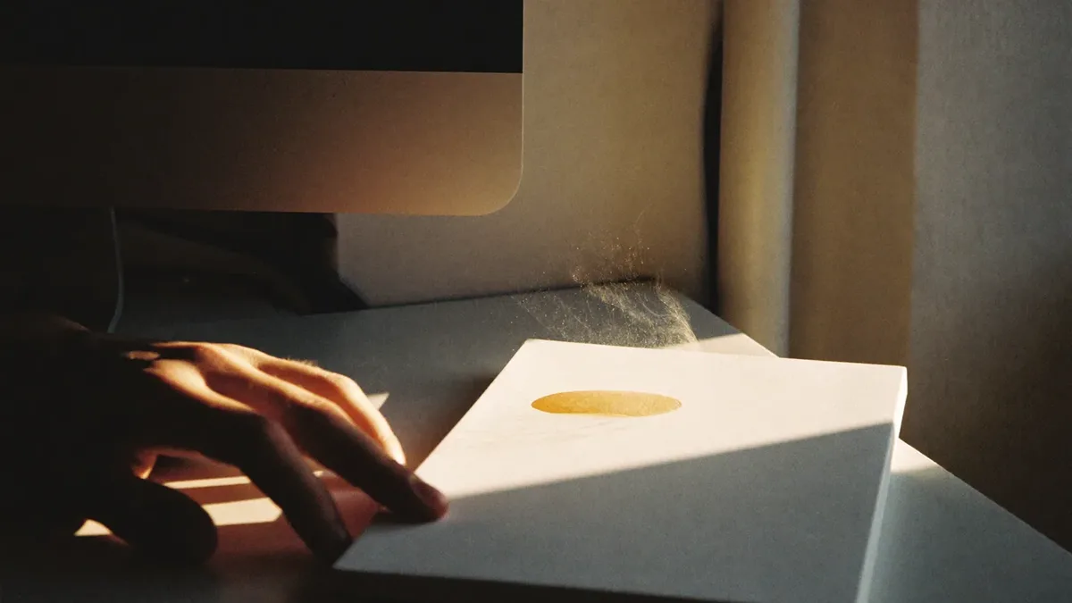 Hand resting beside a notebook at a desk in low evening light