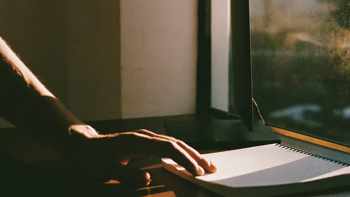 Hand resting beside a notebook at a desk in low evening light