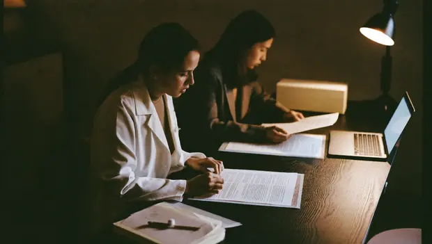 Two colleagues reviewing printed clinical content at a desk