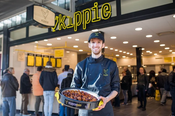 Kippie ondernemer Leender de Wit voor zijn winkel, met kippiepan in de handen